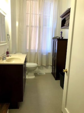 A well-appointed bathroom featuring a toilet, sink, and a mirror that adds a touch of elegance, with a shower stall adorned by a gracefully curtained window that bathes the space in gentle natural light.