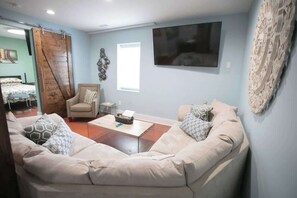 The room features a plush sectional sofa adorned with patterned pillows, centered around a wooden coffee table. A rustic barn door, wall art, and a mounted TV complete the tranquil, stylish living space.