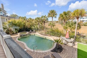 Outdoor pool area with surrounding palm trees, patio furniture, and brick paving. Nearby, a marsh landscape is visible under a partly cloudy sky.