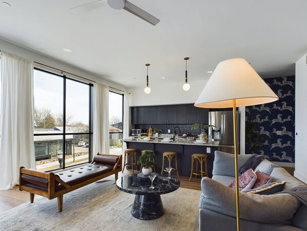 Open floor plan living area with floor-to-ceiling windows, comfortable seating, smart TV, and access to the private balcony.