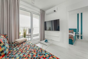 A bright living room with a turquoise sofa, a wall-mounted TV, and floor-to-ceiling windows allowing for ample natural light.

