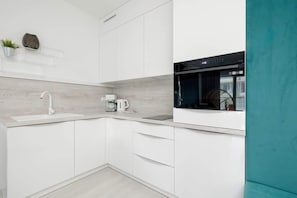 A sleek white kitchen with modern cabinetry, a gray backsplash, and integrated appliances.