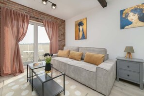 Another view of the living room, featuring a yellow accent sofa, wall artwork, and large windows letting in natural light.

