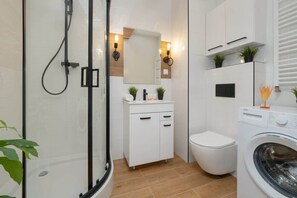 A contemporary bathroom with a glass-enclosed shower, a washing machine, and elegant lighting.

