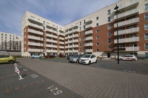 The exterior of a residential complex with modern apartment buildings and a spacious parking area.

