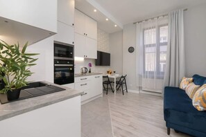An open-concept living and kitchen area featuring a modern blue sofa, a dining table, and bright decor.

