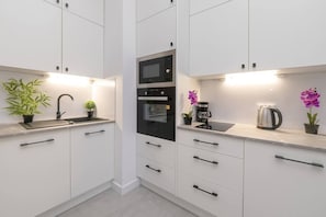 A sleek white kitchen with built-in appliances, black handles, and elegant lighting under the cabinets.

