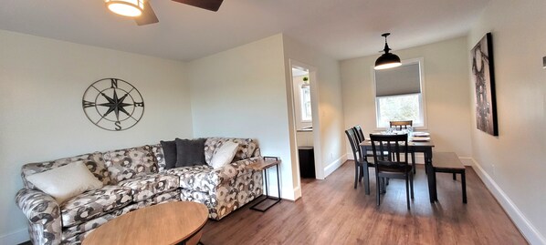 Living and dining room, equipped with large smart TV and desk area.