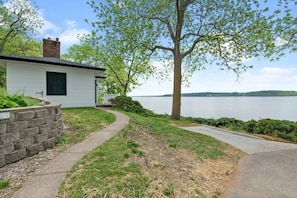 This serene setting features a winding walkway and lush greenery, all framed by a calm lake and clear sky.