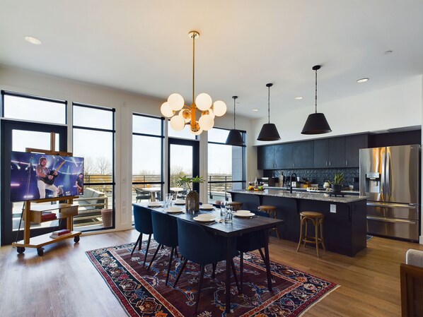 Unit 1: Spacious main living area featuring the fully equipped kitchen boasting stainless steel appliances and a kitchen island offering bar seating, a formal dining table, and a Smart TV.