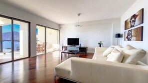 Relax in the spacious living room at Sunset Bay, Funchal. Enjoy a cinematic experience with a large TV and unwind on the expansive sofa, facing south for breathtaking ocean views #sunlight #oceanview #mountainview #funchal