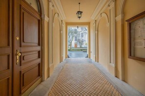 An elegant hallway with an arched ceiling, soft lighting, and intricate wall details, leading to the apartment entrance.

