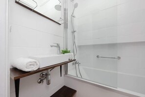 A sleek bathroom with a glass-enclosed shower, white tiles, and a minimalist design.


