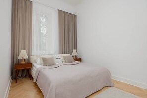A cozy bedroom with a large bed, wooden nightstands, and soft beige curtains, creating a warm and inviting atmosphere.

