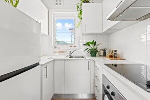 The kitchen is designed with fresh white tones and a clean tiled splashback. There is ample bench space for preparation and a window with natural light.
