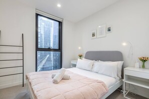 A modern and well-lit bedroom features a plush double bed, built-in wardrobes, bedside tables and a large window.

