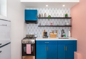 Cook in style at this beautifully designed kitchenette featuring bold blue cabinets, open shelving, and a retro-inspired fridge. Fully stocked with essentials, this space is perfect for preparing meals or enjoying your morning coffee.