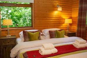 Bedroom with double bed, side tables and lamps window behind bed, wooden panelling