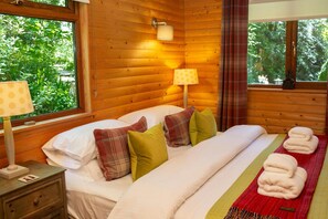 Bedroom with double bed, side tables and lamps window behind bed, wooden panelling