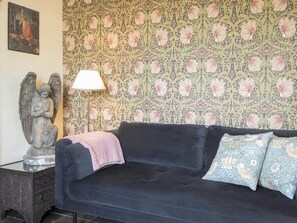 Dark grey velvet sofa. Floral wallpaper. Side table and floor lamp
