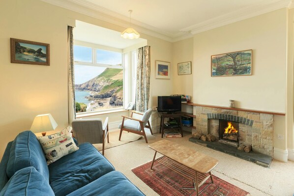 Living room with open fire, sofa, armchairs and sea views