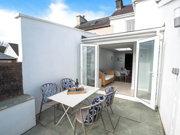 Paved patio with table and four chairs. French doors leading to dining area