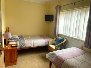 twin beds, bedside table with floor lamp and chair with cushion