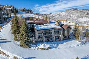 An external view of this luxury Park City vacation rental, with snow covering the roof and a view of the mountain forest behind.