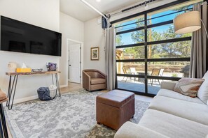 Comfort Meets Entertainment! The Living Room Welcomes You with a Cozy Sofa, Smart TV, and Abundant Natural Light Streaming in Through Large Windows