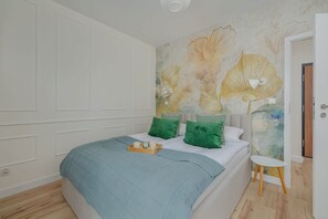 A cozy bedroom with a bed covered in light gray and teal bedding, set against a wallpapered accent wall with botanical designs. The room exudes a calm and serene atmosphere, perfect for relaxation.