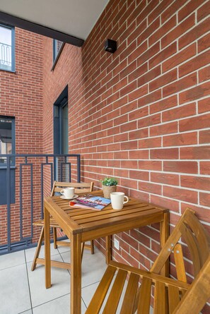 An outdoor patio area featuring a small wooden table and chairs set against a brick wall. The space offers a cozy spot for enjoying outdoor meals or relaxation.