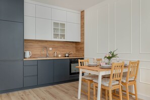 A modern kitchen with dark gray lower cabinets and white upper cabinets, featuring a small wooden dining table. The clean lines and minimalist design offer a sleek, contemporary feel.
