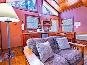 Cozy and inviting, this rustic cabin living room boasts a plush, patterned couch perfect for relaxation. Bathed in warm natural light from large windows, it offers a serene retreat amidst natu