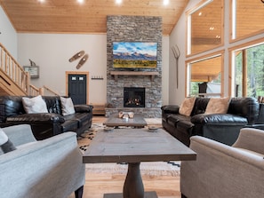 Relax in this warm and inviting living room, featuring a grand stone fireplace, plush seating, and stunning forest views—perfect for unwinding after a day of adventure.