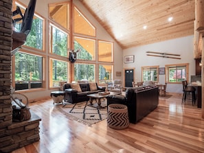 This spacious lodge-style living room is filled with natural light thanks to floor-to-ceiling windows. It offers stunning views of the pines and is the perfect spot to relax comfortably.