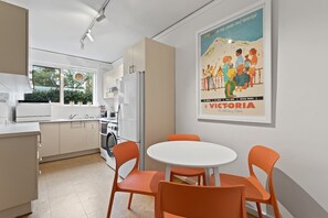 The dining table adjoins the kitchen and has a funky white round table with four vivid tangerine-toned seats. 
