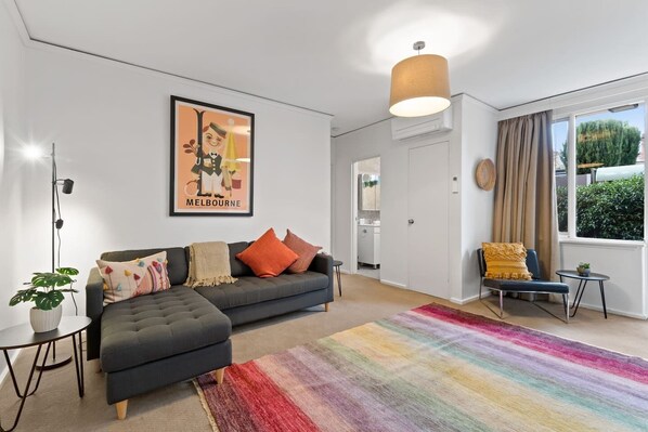 The living room is a fun and vibrant space with retro look wall art, a rainbow rug and bright throw pillows on the cosy chaise lounge.
