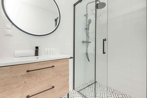 A bright and elegant bathroom featuring a walk-in shower, wooden cabinetry, and geometric floor tiles that add a touch of modern sophistication.