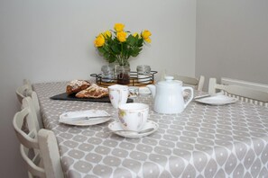 dining table laid for tea, with tea cups, saucers and teapot. Vase with yellow roses