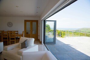 Lounge and dining area with doors open to patio with sea views