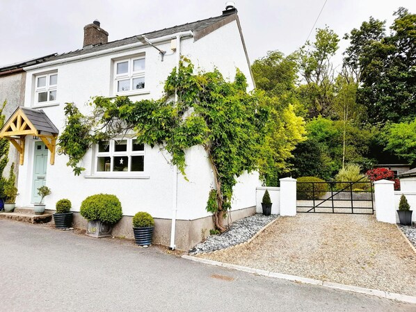 Outside of the cottage with mature wisteria and driveway with parking