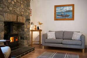 two seater sofa, cushions, side table with ornaments, log fire with brick chimney breast
