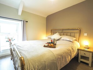 King size bed with tray laid for breakfast on it. Window with vase of flowers