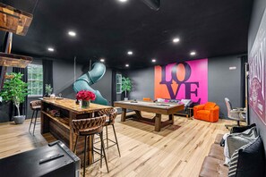 Sophisticated speakeasy with pool table, long dining table, large TV, poker table, and a playful slide