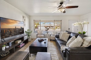 Living room with leather couch, large TV, ceiling fan, & window with blinds