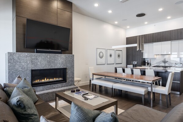 - Modern living room with stone fireplace and mounted flat screen TV  
- Open floor plan connects lounge with dining and sleek kitchen area  
- Bright space designed for comfort and après-ski gatherings