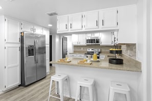 Large kitchen with cabinets, four burner stove and oven, microwave, kettle, large refrigerator, bar and lots of light.