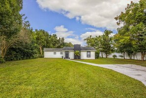 The entrance to the house is surrounded by lush green grass and trees, creating a welcoming and natural setting. The well-maintained lawn and shaded trees offer a picturesque and inviting first impression of the home, blending tranquility with natural beauty.