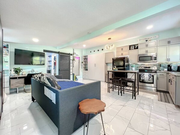 This living room features a comfortable sofa and is conveniently located near the dining area and kitchen. It also includes a desk, providing additional space for work or study, making the area both functional and versatile.