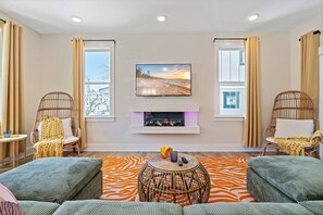 Living room with fire place, TV,; framed by windows and rattan wing chairs